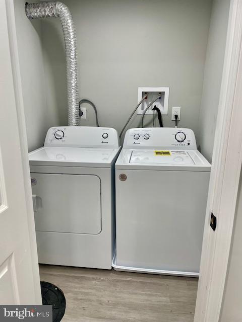 laundry area with washing machine and clothes dryer and light wood-type flooring