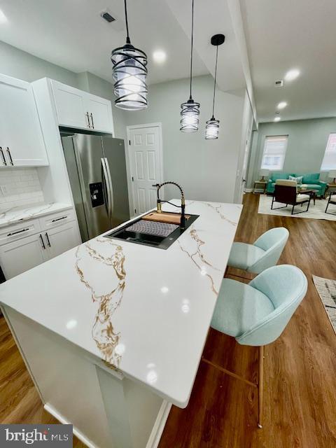 kitchen featuring a kitchen bar, white cabinetry, pendant lighting, and stainless steel refrigerator with ice dispenser