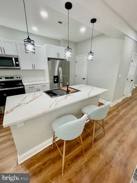 kitchen with a center island with sink, white cabinets, light wood-type flooring, and stainless steel appliances