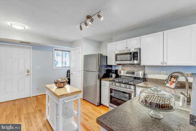 kitchen featuring tasteful backsplash, white cabinets, light hardwood / wood-style floors, and appliances with stainless steel finishes