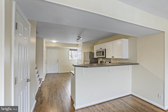 kitchen with stainless steel appliances, kitchen peninsula, hardwood / wood-style floors, a breakfast bar, and white cabinets