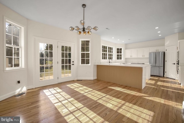 kitchen featuring kitchen peninsula, light hardwood / wood-style flooring, a notable chandelier, white cabinets, and stainless steel refrigerator