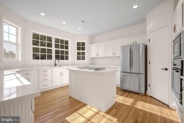 kitchen with appliances with stainless steel finishes, a center island, light hardwood / wood-style floors, and white cabinetry