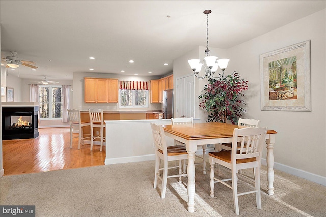 dining room featuring ceiling fan with notable chandelier, a healthy amount of sunlight, a multi sided fireplace, and light wood-type flooring