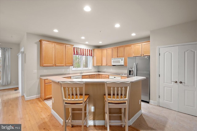 kitchen with a center island, light brown cabinets, white appliances, a kitchen breakfast bar, and light hardwood / wood-style flooring