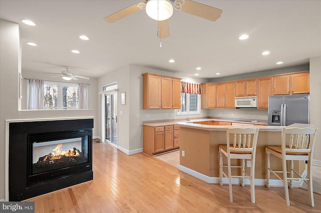 kitchen with a kitchen breakfast bar, a multi sided fireplace, stainless steel refrigerator with ice dispenser, light wood-type flooring, and a kitchen island