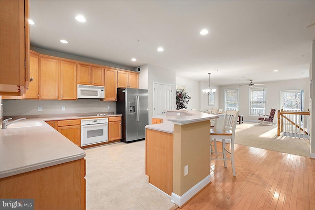 kitchen with a center island, sink, hanging light fixtures, white appliances, and a kitchen bar