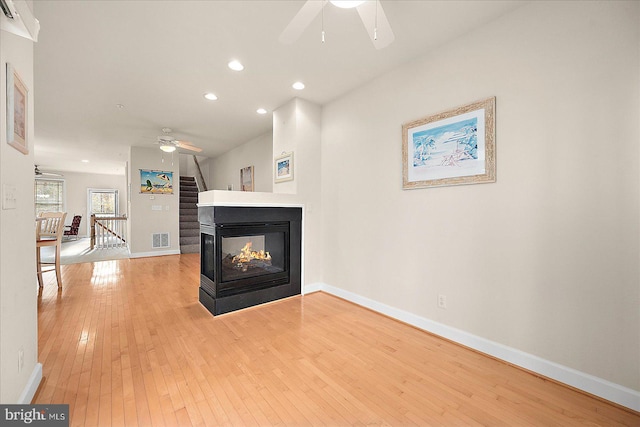 living room with a multi sided fireplace, light hardwood / wood-style floors, and ceiling fan