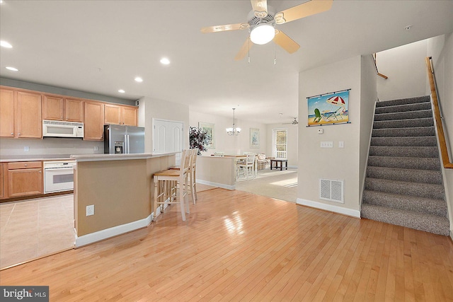 kitchen featuring ceiling fan with notable chandelier, light hardwood / wood-style floors, white appliances, and a kitchen island