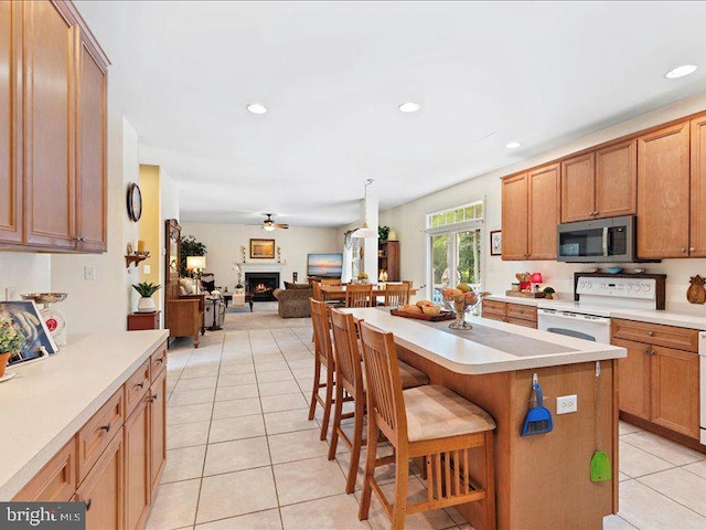 kitchen with ceiling fan, a center island, a kitchen breakfast bar, white range, and light tile patterned floors