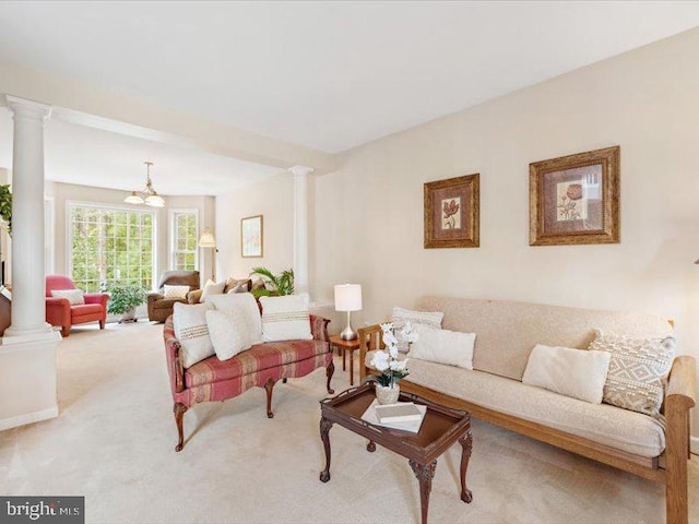 carpeted living room featuring ornate columns and a notable chandelier