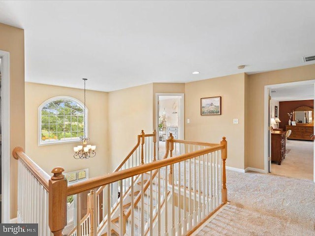 hallway featuring a notable chandelier and light carpet