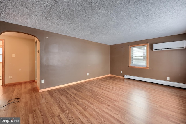 unfurnished room with light hardwood / wood-style floors, baseboard heating, a textured ceiling, and a wall unit AC