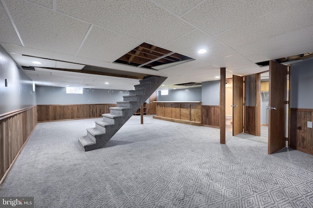 basement with wooden walls, a drop ceiling, and light colored carpet