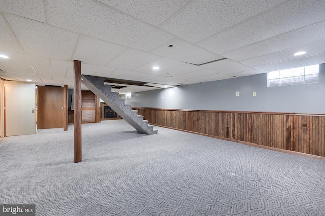 basement with carpet, a drop ceiling, and wood walls