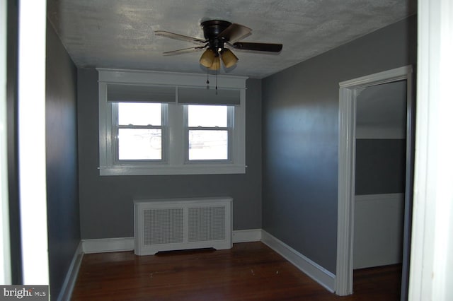 empty room with dark hardwood / wood-style floors, ceiling fan, a textured ceiling, and radiator