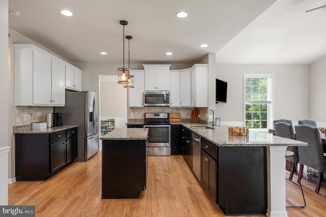 kitchen featuring pendant lighting, light hardwood / wood-style flooring, appliances with stainless steel finishes, tasteful backsplash, and kitchen peninsula