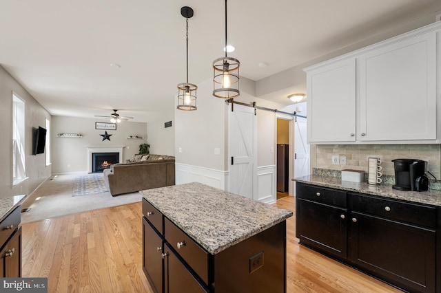 kitchen with a center island, hanging light fixtures, ceiling fan, a barn door, and white cabinetry