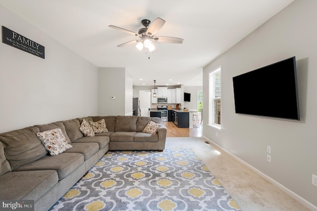 living room with ceiling fan, sink, and light colored carpet