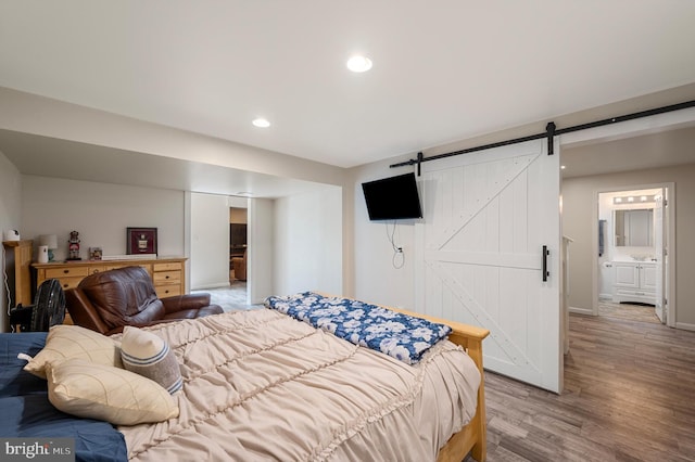 bedroom with a barn door, ensuite bathroom, and light hardwood / wood-style flooring