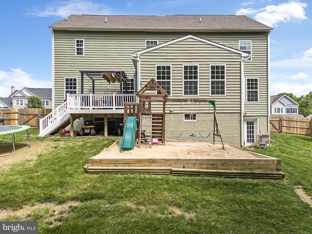 back of house featuring a playground, a yard, a trampoline, and a wooden deck