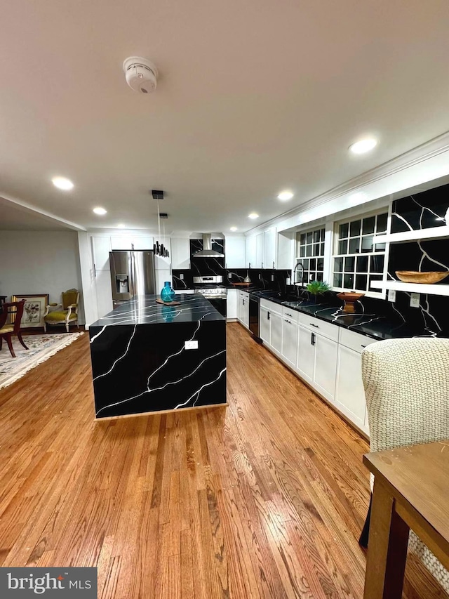 kitchen with wall chimney exhaust hood, decorative light fixtures, white cabinets, a center island, and stainless steel appliances