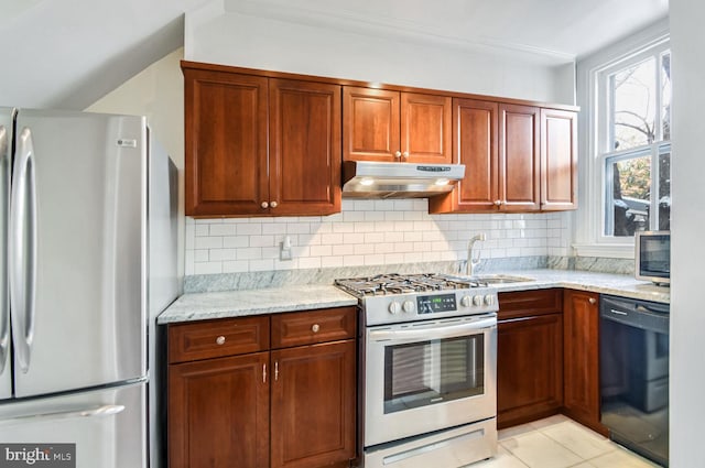 kitchen featuring light stone counters, stainless steel appliances, decorative backsplash, a sink, and under cabinet range hood