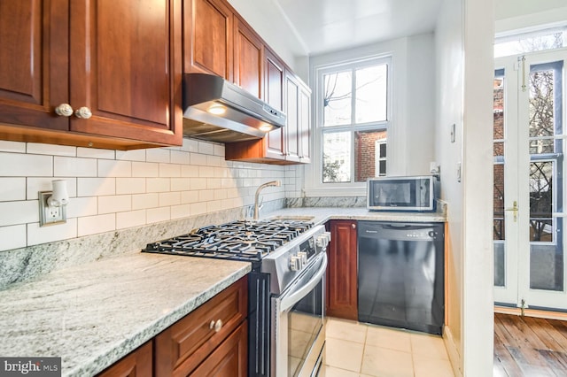 kitchen with light stone counters, light tile patterned flooring, under cabinet range hood, appliances with stainless steel finishes, and backsplash