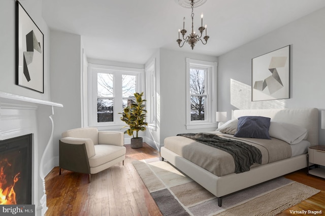 bedroom featuring a warm lit fireplace, wood-type flooring, and a chandelier