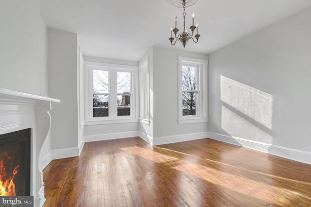 unfurnished living room with a lit fireplace, baseboards, wood-type flooring, and a notable chandelier