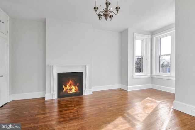 unfurnished living room with a warm lit fireplace, wood-type flooring, baseboards, and a notable chandelier