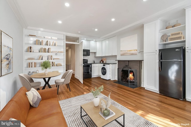 living area with recessed lighting, a fireplace with flush hearth, light wood-style floors, washer / dryer, and crown molding