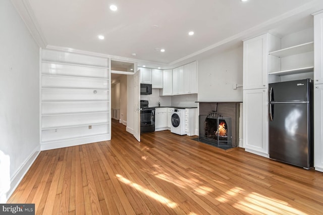 unfurnished living room featuring a warm lit fireplace, washer / dryer, light wood-style flooring, crown molding, and recessed lighting