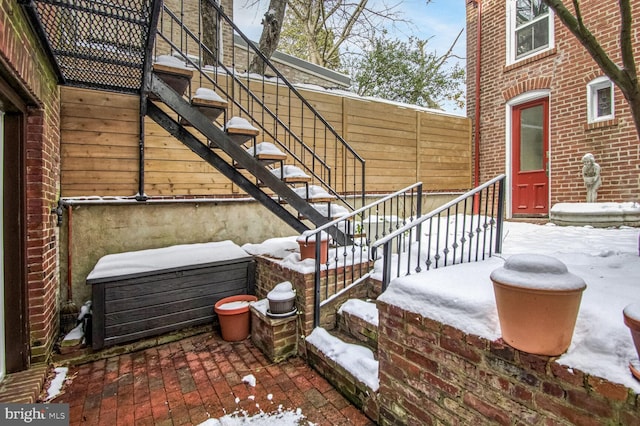 snow covered property featuring stairs, brick siding, and a patio area