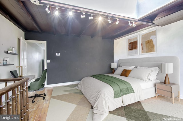 bedroom featuring wood finished floors, beam ceiling, and baseboards