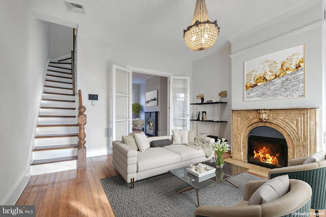 living room with a warm lit fireplace, hardwood / wood-style flooring, visible vents, baseboards, and stairway