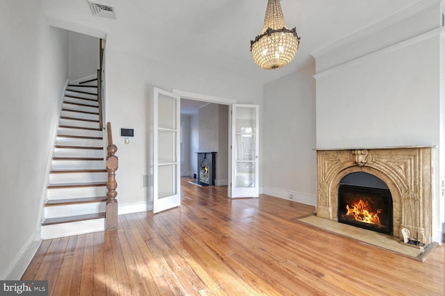 unfurnished living room with a warm lit fireplace, visible vents, hardwood / wood-style floors, and stairs