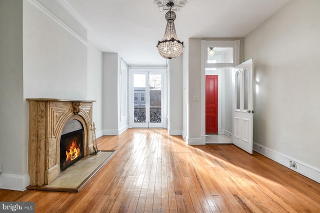 unfurnished living room featuring a warm lit fireplace, hardwood / wood-style floors, crown molding, and baseboards