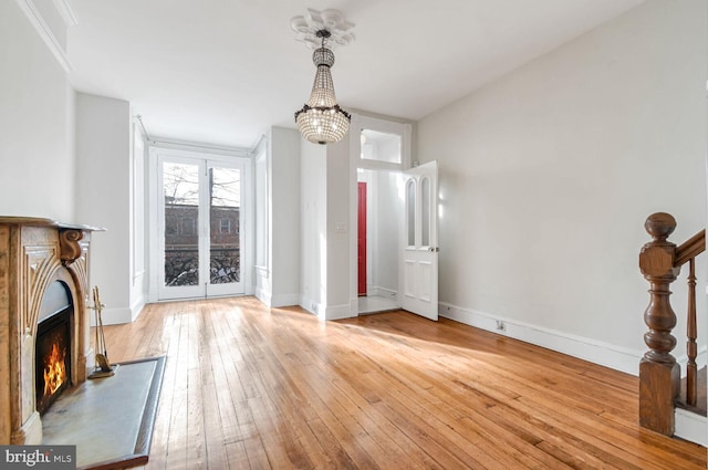 unfurnished living room featuring a lit fireplace, hardwood / wood-style flooring, and baseboards