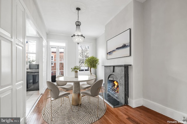 dining space with a lit fireplace, ornamental molding, light wood-style flooring, and baseboards