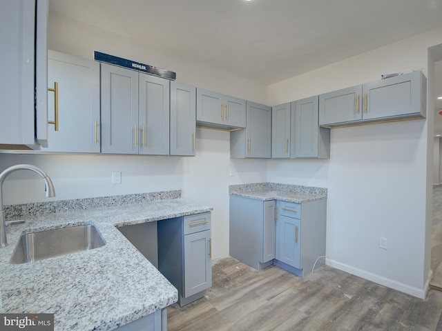 kitchen with light stone counters, sink, and light hardwood / wood-style flooring