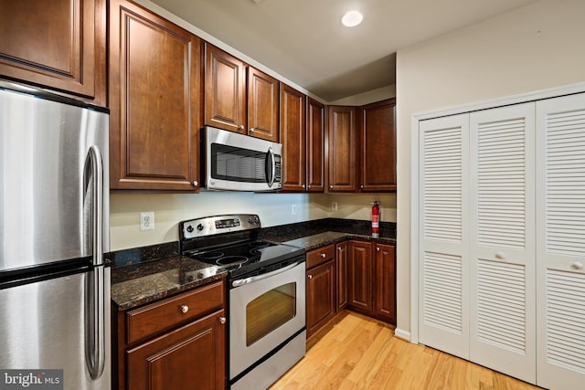 kitchen featuring appliances with stainless steel finishes, light hardwood / wood-style floors, and dark stone counters