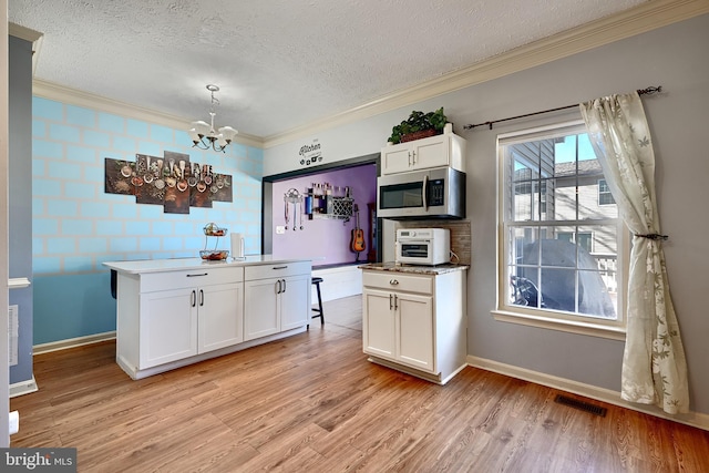 kitchen featuring crown molding, pendant lighting, light hardwood / wood-style flooring, an inviting chandelier, and white cabinets