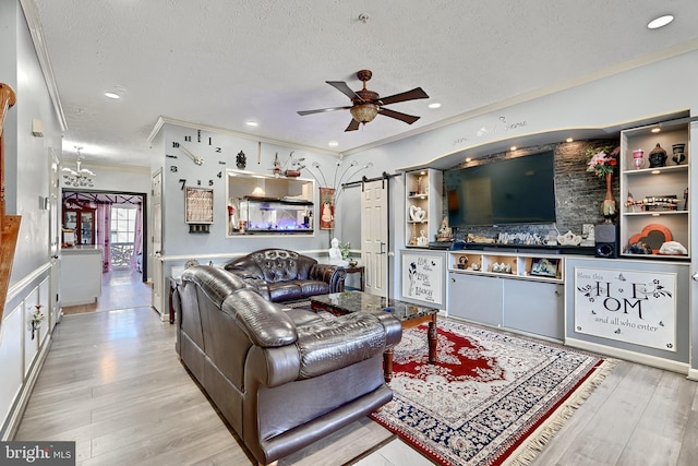 living room with light wood-type flooring, ornamental molding, a textured ceiling, ceiling fan, and a barn door