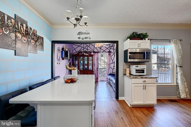 kitchen featuring light wood-type flooring, ornamental molding, a textured ceiling, an inviting chandelier, and white cabinetry