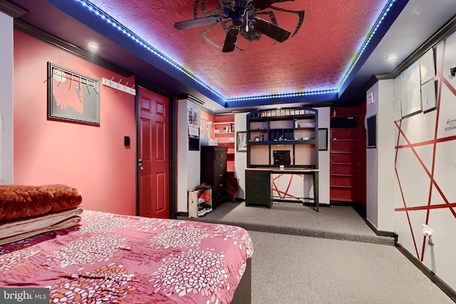 bedroom with ceiling fan, ornamental molding, a textured ceiling, a tray ceiling, and carpet floors