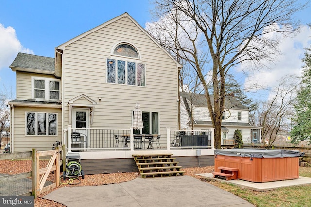 back of house with a deck, a patio area, a shingled roof, and a hot tub