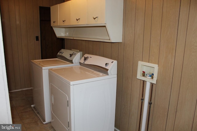 clothes washing area with tile patterned floors, washer and dryer, cabinets, and wooden walls