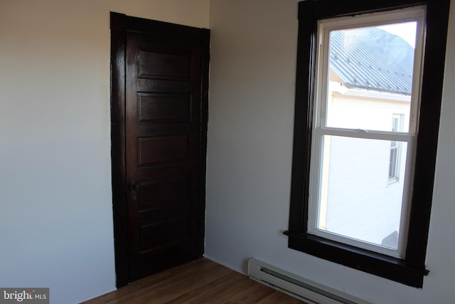 unfurnished room featuring dark wood-type flooring, a baseboard radiator, and a healthy amount of sunlight