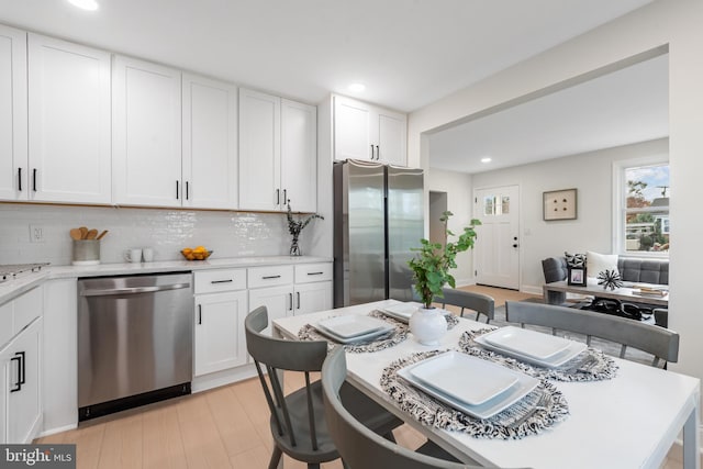 kitchen featuring white cabinets, appliances with stainless steel finishes, light hardwood / wood-style floors, and decorative backsplash